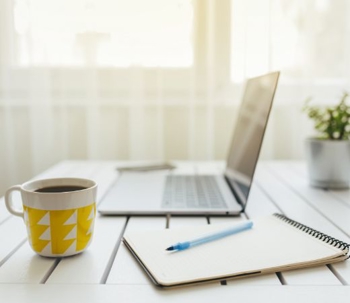 Coffee mug, laptop, and notepad on a desk.